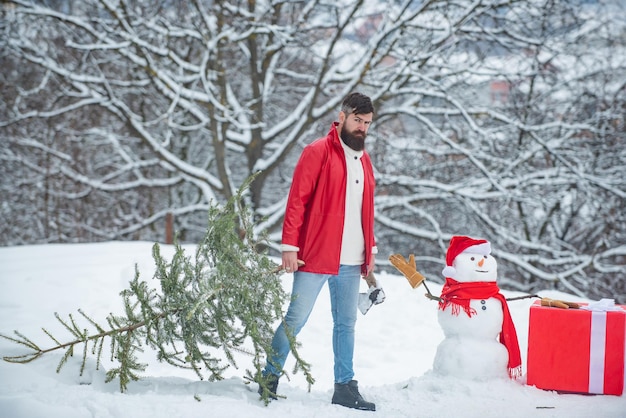Grappige kerstman poseren met bijl en kerstboom man gaat een kerstboom omhakken een knappe l...