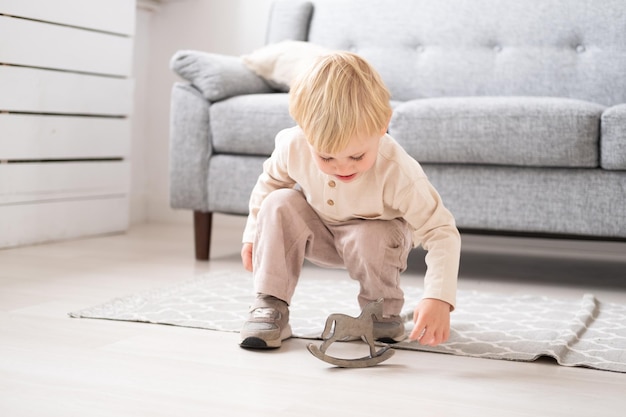 Grappige kind jongen spelen met houten speelgoed paard in moderne woonkamer