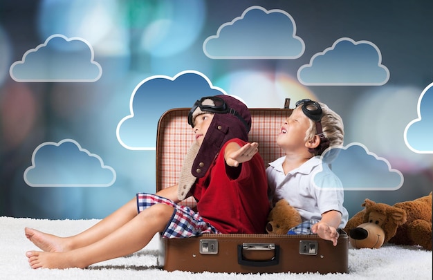 Foto grappige kinderen zitten aan koffer en gek rond op digitale wolken achtergrond