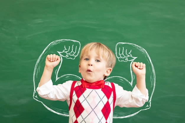 Grappige kindstudent in de klas tegen groen bord. Lichamelijke opvoeding.