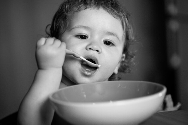 Grappige kleine baby in de keuken die met vingers van bord eet