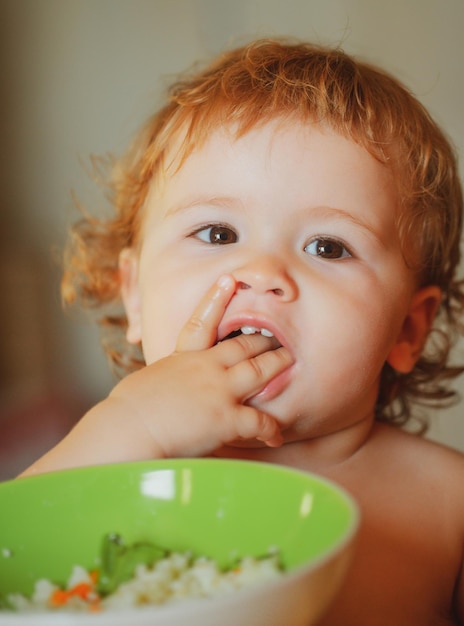 Grappige kleine baby in de keuken die met vingers van bord eet