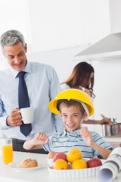 Grappige kleine jongen die bouwvakker draagt ​​tijdens het ontbijt met zijn ouders