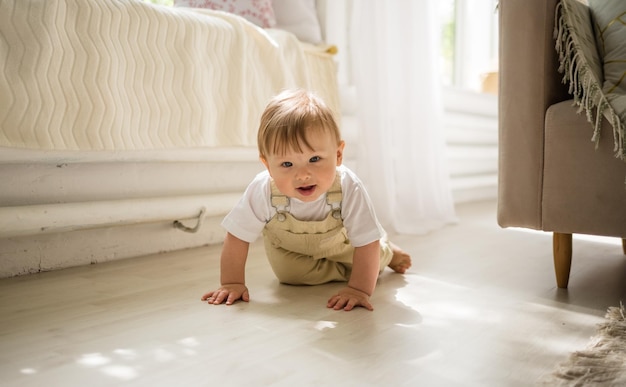 Grappige kleine jongen in beige jumpsuit die op de vloer in de kamer kruipt