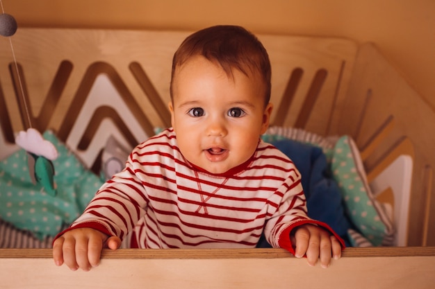 Grappige kleine jongen in gestripte pyjama staat in een houten bed