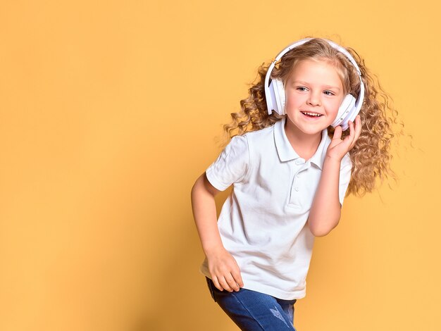 Grappige kleine jongen meisje in wit t-shirt geïsoleerd op gele ruimte. jeugd levensstijl concept. mock up kopie ruimte. luister naar muziek in een koptelefoon, dansend met wapperende haren