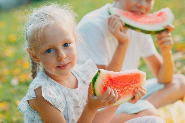 Grappige kleine peuter kinderen broer en zus watermeloen eten op het park. Gelukkige jongen en meisje samen. Jeugd, gezin, gezond dieetconcept.