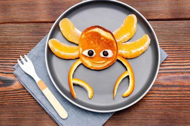 Grappige krab gezichtsvorm snack van pannenkoek oranje op plaat Cute kids childrens baby's zoete dessert gezond ontbijtlunch voedsel kunst op houten backgroundtop weergave