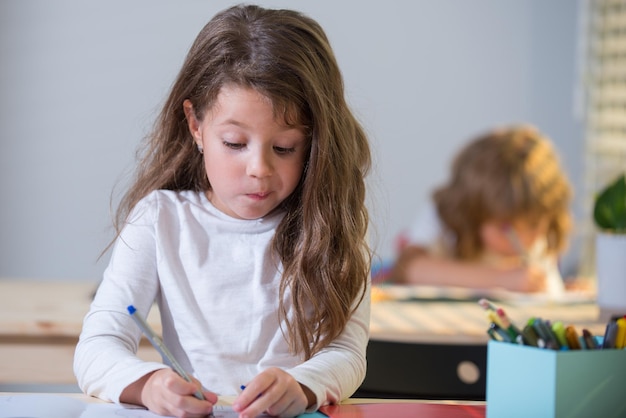 Grappige leerling in de klas op school klein meisje zit aan het bureau in de klas portret van jong schoolmeisje