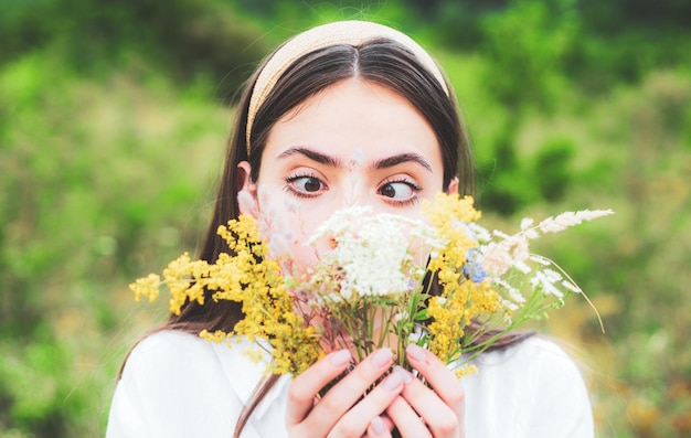 Foto grappige lente jonge vrouw buiten mooie tiener meisje in een veld van witte bloemen leuke gezicht emoties meisje met een boeket van wilde bloemen