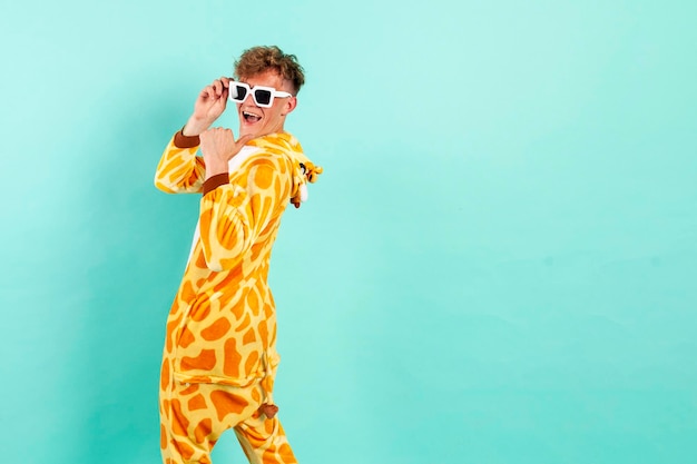 grappige man in oranje giraffe pyjama danst op een feestje in zonnebril en wijst terug op blauwe achtergrond