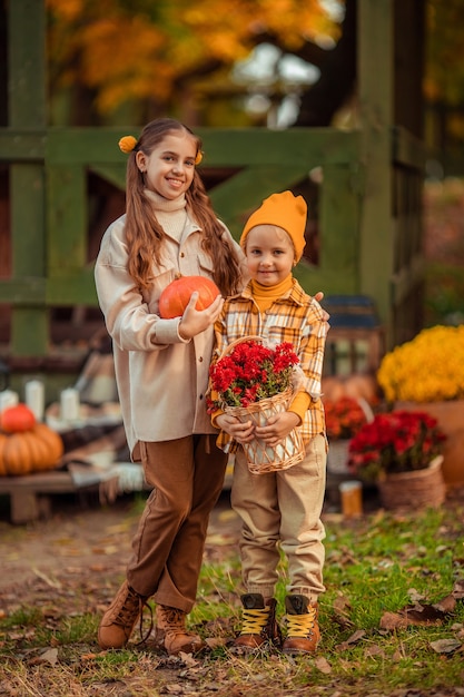 Grappige meisjeszusters in de herfst met pompoenen en bloemen veel plezier