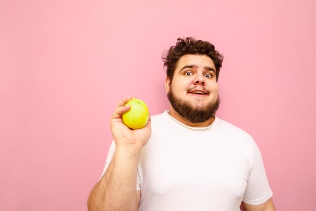 Grappige overgewicht man in witte t-shirt geïsoleerd op een roze achtergrond met een groene appel