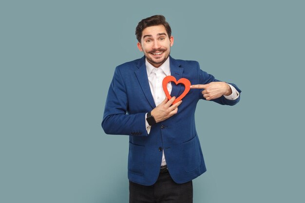 Grappige positieve optimistische man met snor staande wijzend op hartfiguur kijkend naar de camera