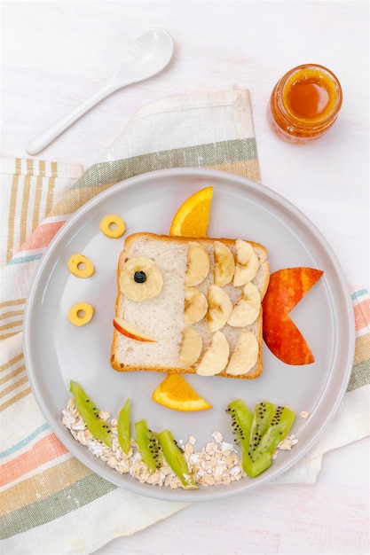 Grappige schattig vis vorm sandwich toast brood met banaan appelsinaasappelhoning kinderen kinderen baby's zoete dessert gezond ontbijt lunch eten kunst op platewooden achtergrond close uptop uitzicht