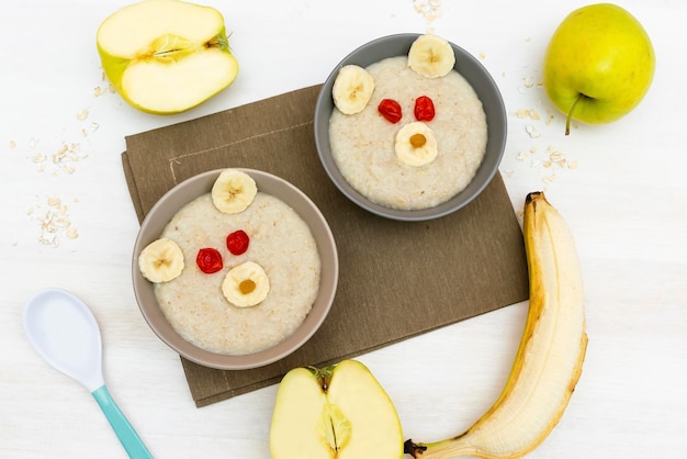 Grappige schattige kinderen Childrens baby's gezond ontbijt lunch havermoutpap in kom eruit als berengezicht versierd met appel banaan gedroogde bessen fruit dessert voedsel kunst op witte houten tafel