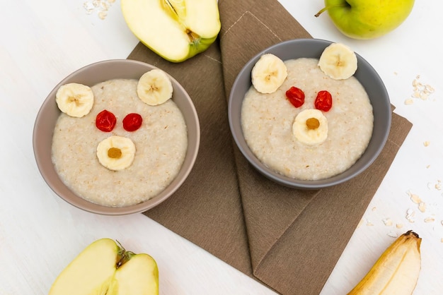 Grappige schattige kinderen Childrens baby's gezond ontbijt lunch havermoutpap in kom eruit als berengezicht versierd met appel banaan gedroogde bessen fruit dessert voedsel kunst op witte houten tafel