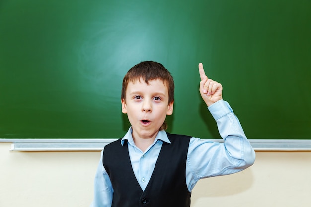 Grappige schooljongen in de buurt van het groene schoolbestuur in de klas. Kind van de basisschool. Terug naar school.