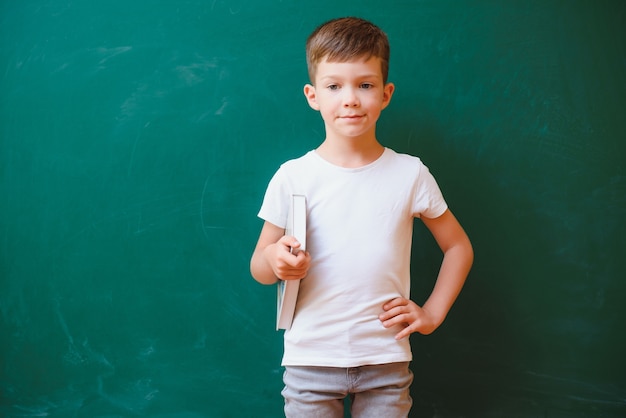 Grappige schooljongen in de buurt van het groene schoolbestuur in de klas. lagere school. terug naar school.