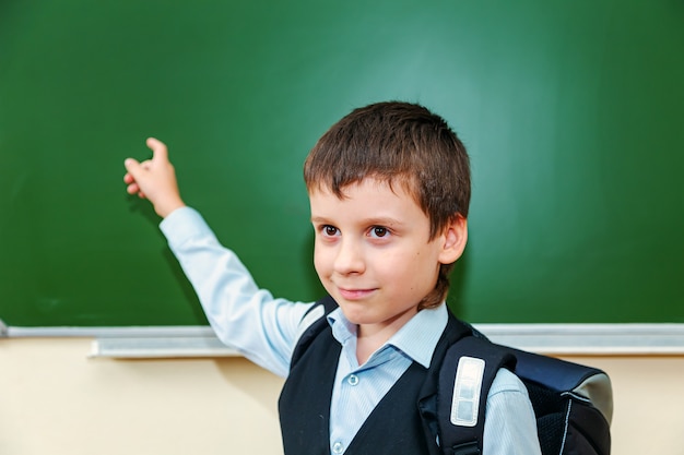 Grappige schooljongen wijst naar het bord Basisschoolkind met tas Terug naar school