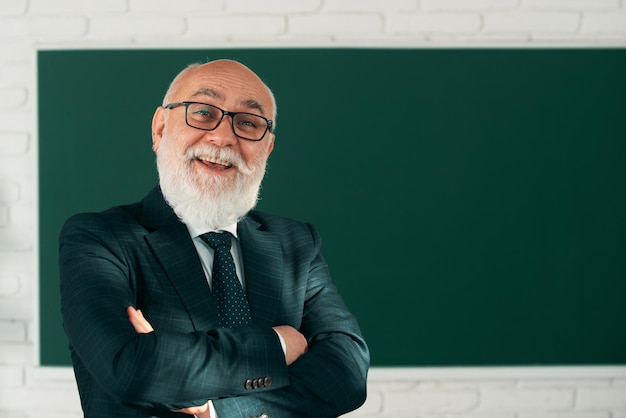 Foto grappige senior professor portret van gelukkige senior leraar met gekruiste armen staande tegen krijtboar