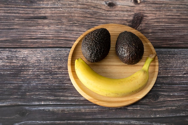 Grappige snuit van banaan en avocado op een houten plaat op een houten ondergrond.