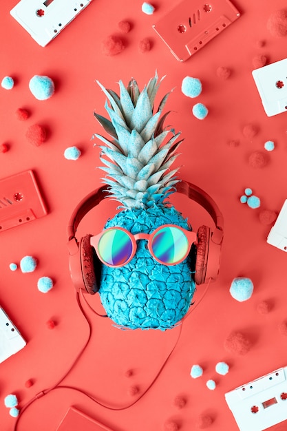 Grappige turquoise ananas in zonnebril en koptelefoon op versierd rood papier