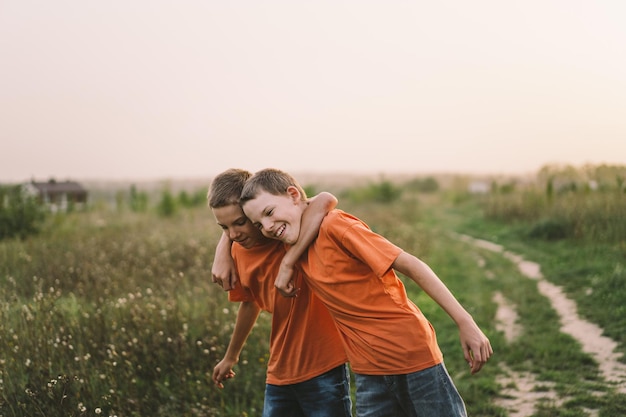 Grappige tweelingbroer jongens in oranje t-shirt buiten spelen op veld bij zonsondergang Happy children lifestyle