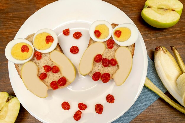 Grappige uil gezicht sandwich toast brood met kippeneieren appel banaan gedroogde bessen op plaat schattige kinderen kinderen baby's zoete dessert ontbijt lunch voedsel kunst op houten backgroundtop weergave