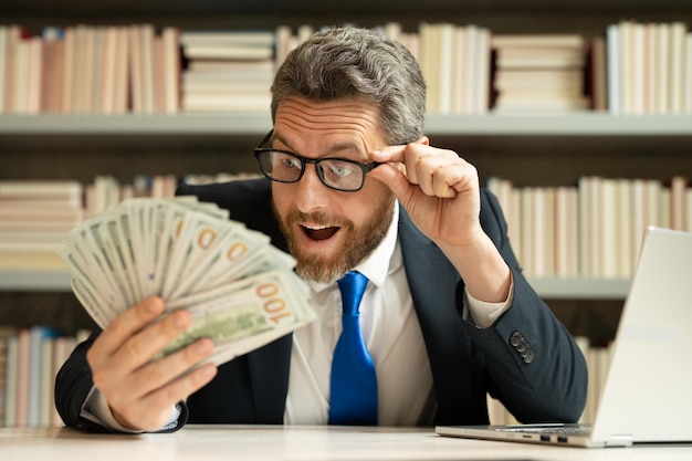 Foto grappige verbaasd opgewonden zakenman houdt geld in kantoor rijke man in pak met geld dollarbiljetten succ