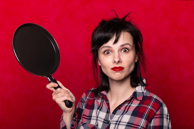 grappige vrouw met een koekenpan in handen koken rode achtergrond