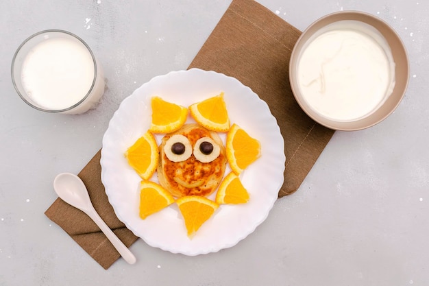 Grappige zon gezichtsvorm snack van pannenkoekorange op plaat schattige kinderen kinderen baby's zoete dessert gezond ontbijtlunch eten kunst met melk en zure room op grijze betonnen achtergrond bovenaanzicht