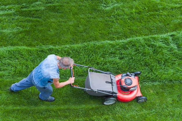 Grasmaaier maait groen gras, de tuinman met een grasmaaier werkt in de achtertuin, bovenaanzicht