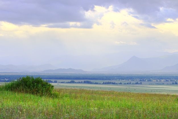 Photo grassy steppe among blue mountains in fog, cloudy sunset sky. siberia, russia