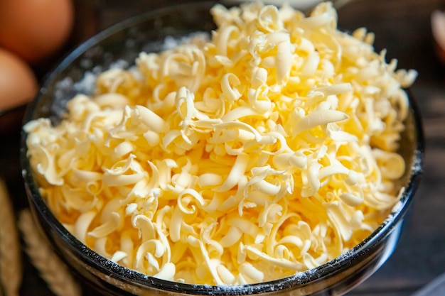 Grated butter for baking on table. Baking ingredients for shortbread pastry: grated butter, flour, eggs, sour cream close up on wooden background.