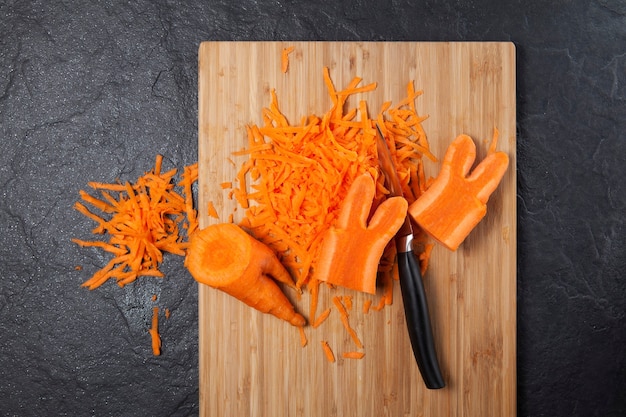 Фото Натертая морковь на разделочной доске. модный тренд - есть деформированные и некрасивые овощи. уменьшение пищевых отходов.
