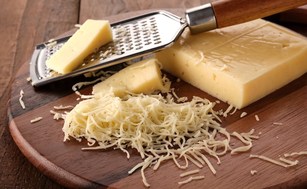 Grated cheese and grater on a wooden board.