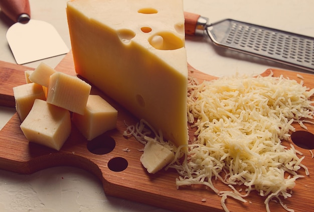 Grated cheese Maasdam on a cutting board grater and cheese knife closeup no people