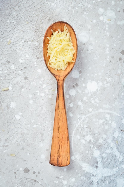 Grated cheese in a spoon. Hard parmesan cheese. Top view. On a stone background.