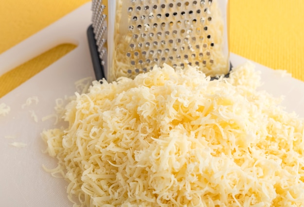 Photo grated cheese on a white plastic cutting board. close-up