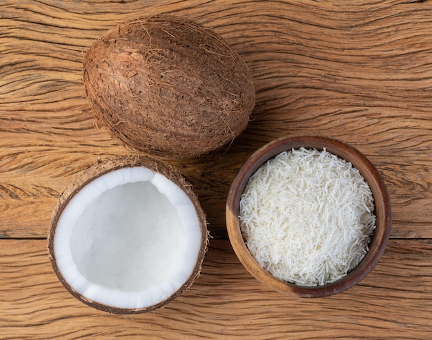 Grated coconut flakes in a bowl with fruit over wooden table