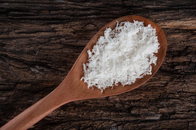 Grated dry coconut in wooden spoon on rustic wooden background