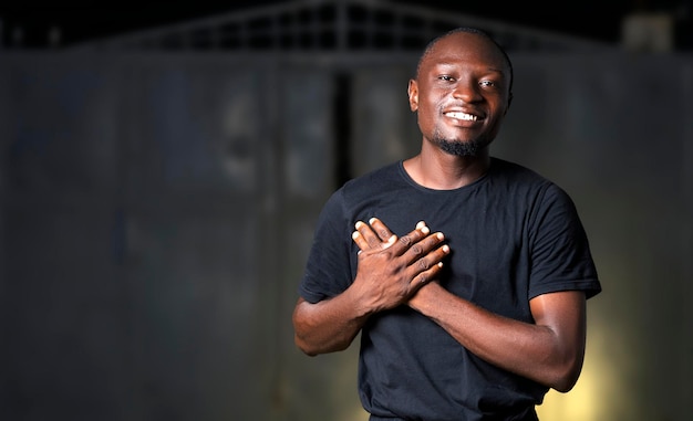 Grateful happy young black african man holding hands close to chest