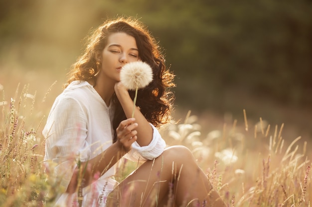 Gratis gelukkige vrouw genieten van de natuur. Schoonheid meisje buiten. Vrijheidsconcept. Schoonheidsmeisje met paardebloem, zonnig bloemengebied. Zonnestralen. Plezier en tederheid. Portretfoto