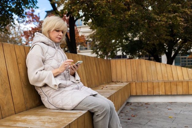 Gratis wifi in het stadspark, een volwassen blanke vrouw zit op een bank en gebruikt een smartphone-kopi