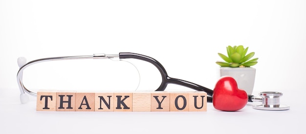 Gratitude expressing to all doctors. close up panoramic frame\
view photo of doctor tools red small heart and wooden blocks with\
inscription isolated white backdrop