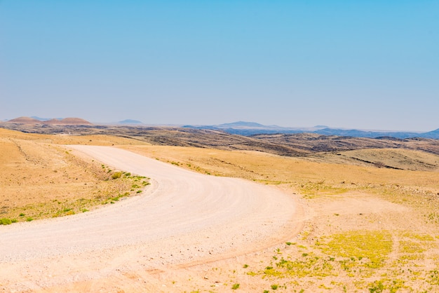 Gravel winding road crossing the colorful Namib desert, in the majestic Namib Naukluft National Park, best travel destination in Namibia, Africa.