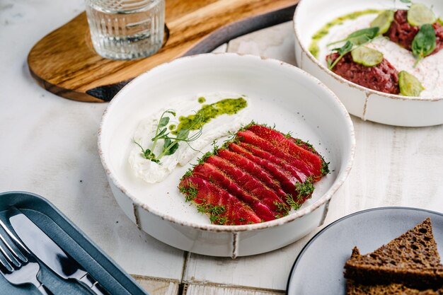 Gravlax salmone essiccato scandinavo con mousse di feta su piatto bianco e tartare di vitello con salsa al tartufo e cetriolo sottaceto