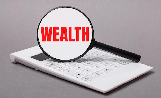On gray background black calculator and magnifier with text WEALTH Business concept
