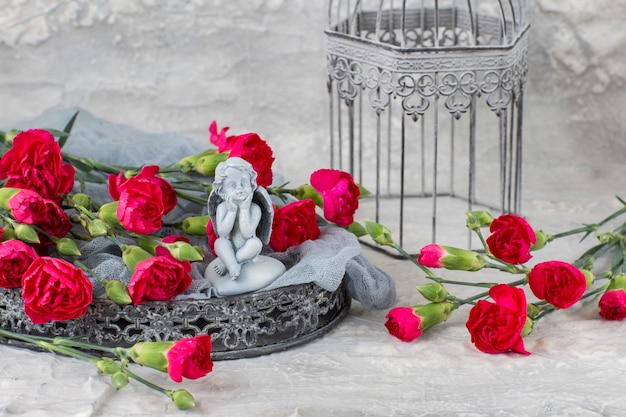 on a gray background bright carnations on a gray tray, a cage and a figure of an angel